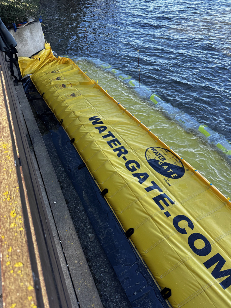 Batardeau souple WA-2850 installé contre la culée nord de la passerelle du Gaou avec lestage par sacs de sable en milieu marin.