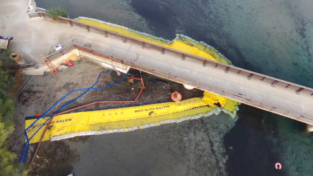 Vue aérienne d’un batardeau souple installé autour de la passerelle du Gaou avec opérations de pompage en cours dans la lagune.