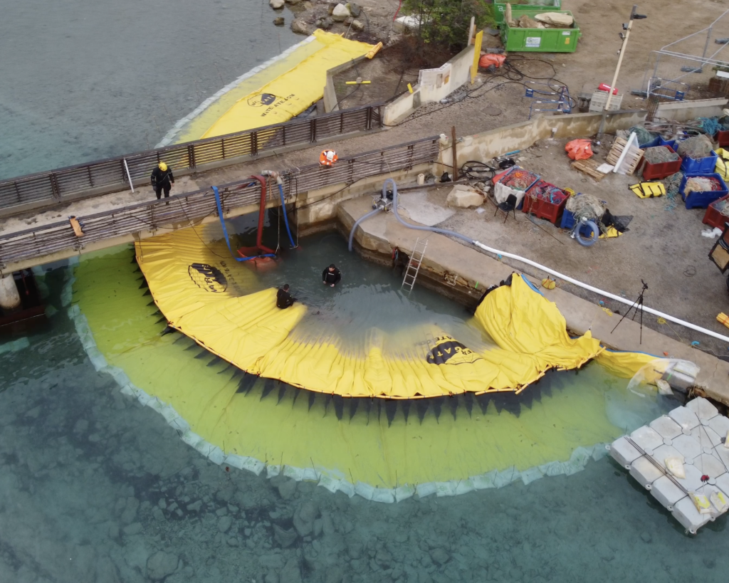 Vue par drone d’un batardeau souple en arc de cercle installé en milieu marin au début des opérations de pompage.